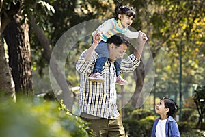 Father carrying daughter on shoulders and holding hands of his son at park