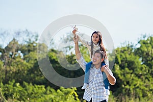 Father and carrying an excited girl on shoulders having fun and enjoying outdoor lifestyle together playing aircraft toy