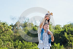 Father and carrying an excited girl on shoulders having fun and enjoying outdoor lifestyle together playing aircraft toy