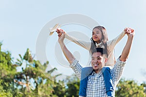 father and carrying an excited girl on shoulders having fun and enjoying outdoor lifestyle together playing aircraft toy