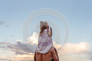 Father carrying his little daughter on shoulders with blue sky background. Happy loving family. Father and daughter