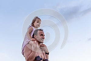 Father carrying his little daughter on shoulders with blue sky background. Happy loving family. Father and daughter