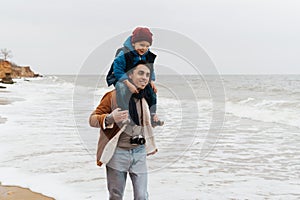 Father carrying on shoulders his son while spending fun time together on beach