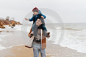 Father carrying on shoulders his son while spending fun time together on beach