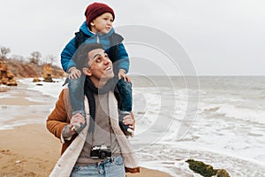 Father carrying on shoulders his son while spending fun time together on beach