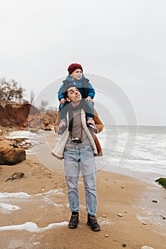 Father carrying on shoulders his son while spending fun time together on beach