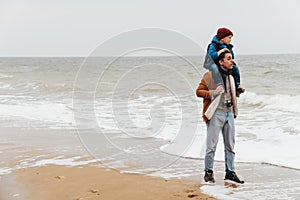 Father carrying on shoulders his son while walking together on beach