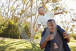 Father Carrying Son On Shoulders As They Walk In Park