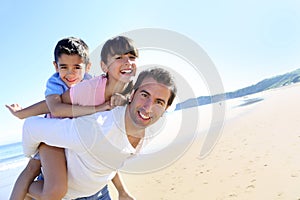 Father carrying two children on his back on the beach