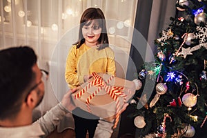 Father celebrates Christmas with his daughter by the beautiful Christmas tree