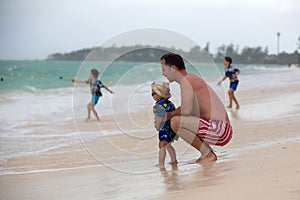 Father and child, boys, having fun on ocean beach. Excited children playing with waves, swimming, splashing happily