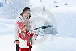 Father and child brushing off car in winter.