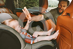 Father with child in car on road trip high five hands baby sitting in safety seat