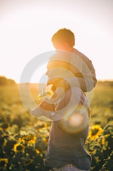 Father with child in a field of blooming sunflowers on sunset. Father`s day