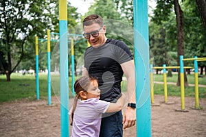 Father with child girl doing pull-ups on workout outdoor area. Healthy active lifestyle, happy family time. Modern
