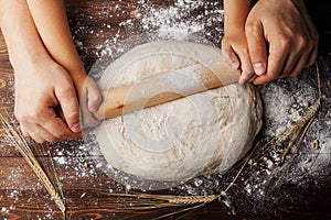 Father and child hands making the dough with flour, rolling pin and wheat ears on rustic wooden table top view.