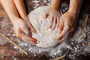 Father and child hands prepares the dough with flour, rolling pin and wheat ears on rustic wooden table from above.