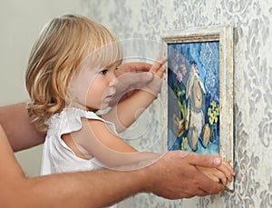 Father and child hanging picture on the empty wall