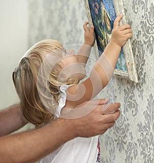 Father and child hanging picture on the empty wall