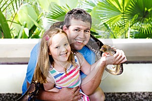 Father and child hold and feed python snake at zoo