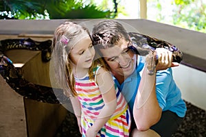 Father and child hold and feed python snake at zoo