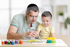 Father and child paint together. Dad teaches son how to paint correct and beautiful on paper. Family creativity and