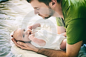 Father and child on a white bed. Father and baby boy in diaper playing in sunny bedroom. Father makes gymnastics for his newborn b