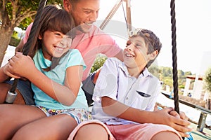 Father And Children Having Fun On Swing In Playground