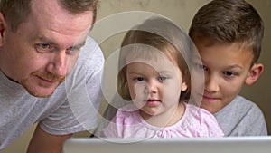 Father and children look at laptop, point to it and laugh