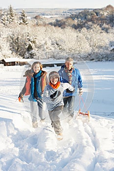 Father And Children Pulling Sledge Up Snowy Hill