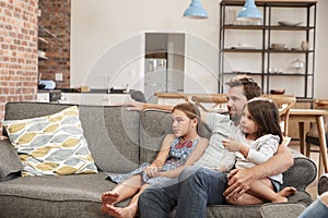 Father And Children Sit On Sofa In Lounge Watching TV