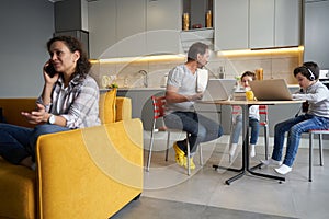 Father with children at table while mother chatting on smartphone