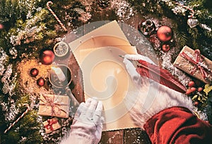 Father Christmas writing a seasonal letter using a vintage feather quill pen on old yellowed paper surrounded by Xmas decorations