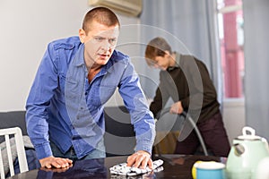 Father cleans the table with a rag while son vacuums room