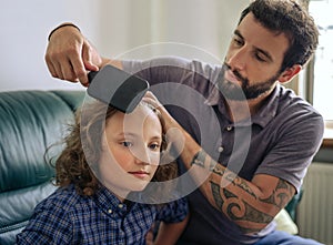 Father combing his young son`s long curly hair at home
