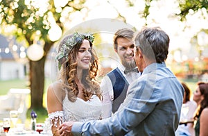 A father congratulating bride and groom at wedding reception in the backyard.