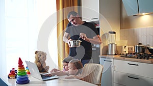 Father cooking in the kitchen remote work. Baby twins playing with laptop in the kitchen. Father working at home in the