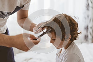 Father cuts her son hair in the room. Family during quarantine, Scissors and a comb in male hands