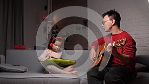 father dad plays guitar with his daughter playing synthesizer, electric piano