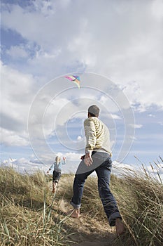 Father and daughter (5-6) flying kite on dunes