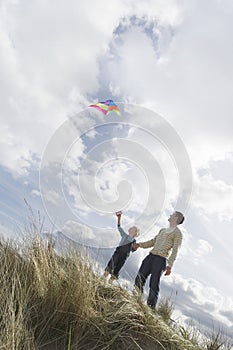 Father and daughter (5-6) flying kite on dunes