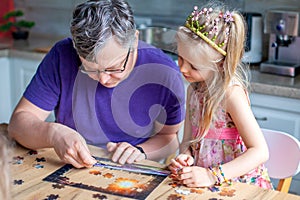 Father and daughter assemble the puzzle while sitting at the table. Games during rain and bad weather, quarantine. Family relaxing