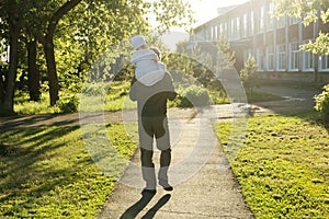 Father with daughter baby on shoulders walking away in park at sunny day. Family authentic lifestyle