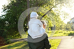 Father with daughter baby on shoulders walking away in park at sunny day. Family authentic portrait
