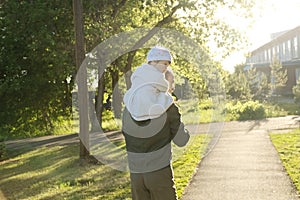 Father with daughter baby on shoulders walking away in park at sunny day. Family lifestyle portrait