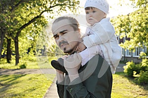 Father with daughter baby on shoulders walking in park at sunny day. Family authentic portrait