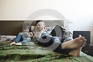 Father and daughter in casual denim clothes are sitting on bed together. The girl having fun writing or drawing while the father