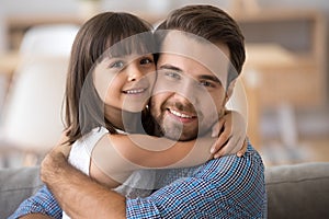 Father and daughter embracing sitting on couch looking at camera