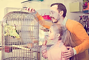 Father and daughter excited to see green parrot in pet shop