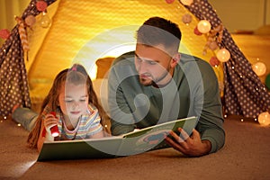 Father and daughter with flashlight reading book